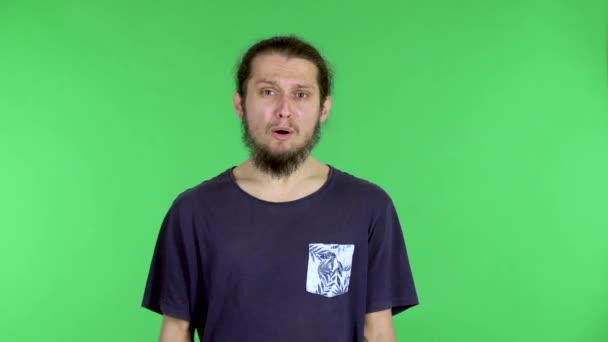 Retrato de um homem, posando em uma camiseta preta em uma tela verde no estúdio. O tipo diz algo emocionalmente, agarra a cabeça com a mão, pensa e encontra uma solução, uma ideia. Fechar. — Vídeo de Stock