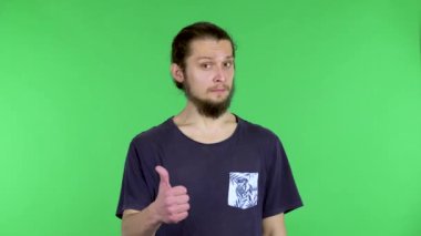 Gülümseyen genç bir adamın portresi iki baş parmak işareti gösteriyor. Stüdyoda yeşil ekranda siyah tişörtlü sakallı adam. Kapat..