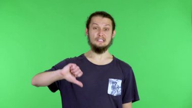 Memnun olmayan genç bir adam, iki parmağını kaldırmış ve hayal kırıklığı içinde başını sallıyor. Reddetme tepkisi, reddetme, huysuz adam. Stüdyoda yeşil ekranda bir adam var. Kapat..
