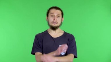 Ciddi bir genç adam dur demek için kollarını kavuşturur ve dur der ve hayır. Stüdyoda siyah tişörtlü, sakallı, siyah saçlı bir adam yeşil ekranda. Kapat..