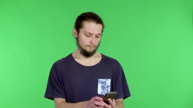 Koyu saçlı, sakallı bir adam elinde akıllı bir telefon tutuyor ve video görüşmesi yapıyor. Adam mutlu bir şekilde müfettişi selamlar, elini sallar. Adam stüdyoda yeşil ekranda poz veriyor. Kapat..