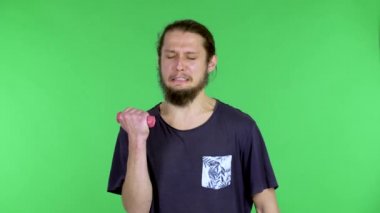Bir adam küçük pembe halterlerle egzersiz yapıyor. Zayıf bir insan son kalan gücüyle kaslarını sallar. Komiklik, mizah. Stüdyodaki yeşil ekrandaki adam. Kapat..