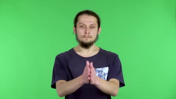 En mørkhåret ung mann i svart T-skjorte holder håndflatene sammen i en bønnemesse. En mann i studio på en grønn skjerm. Lukk. – stockvideo