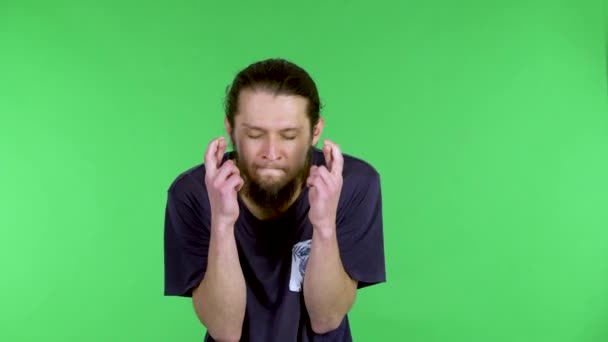 Blanke hoopvolle, opgewonden man houdt zijn vingers gekruist en doet een wens, boos als het niet uitkomt. Een man met een baard in een zwart shirt in de studio op een groen scherm. Sluiten.. — Stockvideo