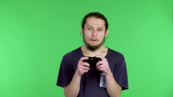 Портрет напряженного молодого человека, играющего в видеоигру с беспроводным контроллером, расстроенного потерей. Темноволосый бородатый мужчина в чёрной футболке в студии на зелёном экране. Закрыть. — стоковое видео