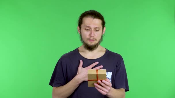 Ein dunkelhaariger Mann öffnet langsam die Geschenkbox, faltet die Geburtstagsüberraschung auf und drückt sein Erstaunen über das Geschenk aus. Der Typ im Studio auf einer grünen Leinwand. Nahaufnahme. — Stockvideo