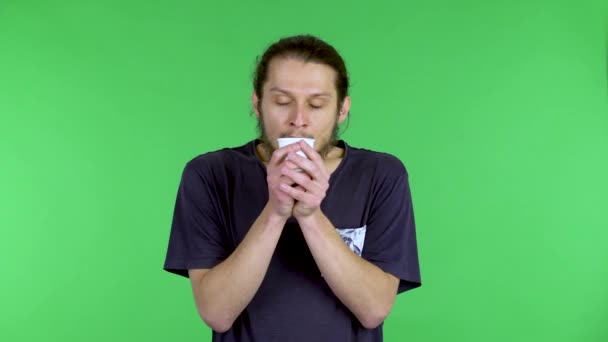 Un retrato de un hombre moreno, barbudo sosteniendo una taza de café, inhala el olor del café aromático y toma un sorbo de la bebida vigorizante. Un hombre en el estudio en una pantalla verde. De cerca.. — Vídeo de stock