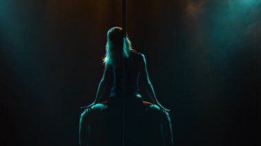 Striptiz yapan seksi zayıf kadın ve gece kulübünde bir direğin üzerinde dönen. Güzel sarışın striptizci, neon ışıkla sahnede erotik hareketler yapıyor. Siluet. Kapat..