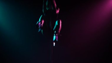 Şehvetli sarışın direğe tırmanıyor, sicim yapıyor ve cinsel olarak iniyor. Direk Dansı. Karanlık stüdyoda duman ve neon ışıkla çekilmiş. Parlak mavi ve mor ışık efektleri. Siluet. Kapat..