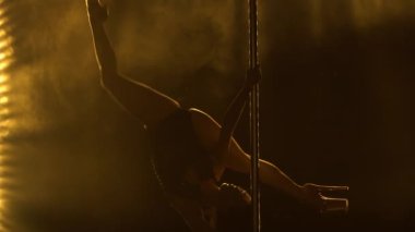 Egzotik direk dansı. Çekici kız, sarı neon ışıkları olan karanlık dumanlı bir stüdyoda bir direğin üzerinde numaralar ve dönüşler yapıyor. Siluet. Kapat..