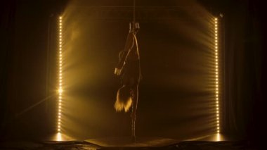 Erotik iç çamaşırlı güzel sarışın direğe tırmanıyor, sicim yapıyor ve cinsel olarak aşağı iniyor. Tüm ihtişamıyla Direk Dansı. Duman ve sarı ışıkla karanlık bir stüdyoda çekildi. Siluet. Yavaş çekim.