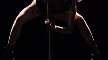 Siyah bir stüdyonun arka planında direğin yanında dans eden genç seksi zayıf kadın. Sahnede baştan çıkarıcı, neredeyse çıplak bir striptizci. Sanat, dans, spor konsepti. Kapatın. Yavaş çekim.