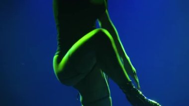 Profesyonel bir striptiz dansçısı tarafından yapılan tutkulu direk dansı. Genç bir kadın, karanlık bir stüdyoda arka planda çok renkli ışıkların karşısında dans ediyor. Siluet. Kapatın. Yavaş çekim.