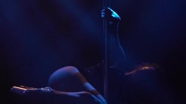 Sütunlu güzel zayıf kadın. Siyah arka planda ışık flaş ışıklarıyla direkte dans eden kadın dansçı. Güçlü ve zarif bir kadın direğin üzerinde dans eder. Siluet. Kapatın. Yavaş çekim.