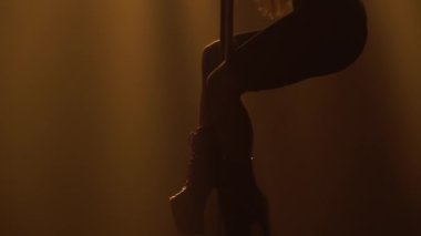 Egzotik direk dansı. Çekici kız, sarı neon ışıkları olan karanlık dumanlı bir stüdyoda bir direğin üzerinde numaralar ve dönüşler yapıyor. Siluet. Kapatın. Yavaş çekim.