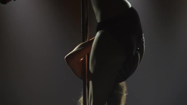 Professional pole dancer performs tricks while spinning on a pole. Stripper erotically moves on a pole in a dark studio with bright lights. Erotic dance, strip show. Silhouette. Close up. Slow motion. — Stock Video