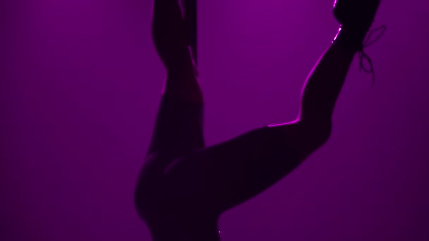Bailarina de polo entrenando cerca de pilón sobre fondo de luces púrpura. Una hermosa hembra joven hace danza de poste, se para las manos y mueve eróticamente sus caderas. Silueta de bailarina. De cerca. Movimiento lento. — Vídeos de Stock