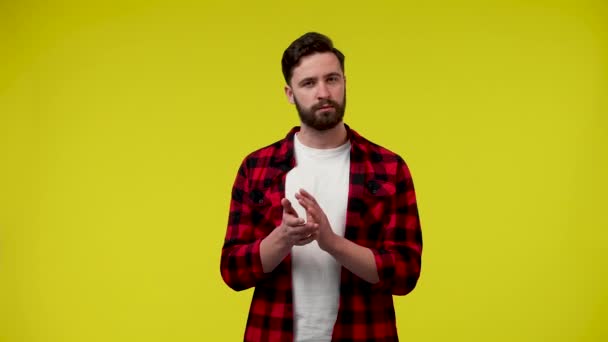 Retrato de un hombre aplaudiendo con las manos en el fondo amarillo del estudio. El primer plano de un tipo sonriente mira a la cámara, asiente con la cabeza con aprobación y aplaude. Cámara lenta lista 59.97fps. — Vídeos de Stock