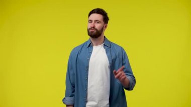 Adam, tasvip etmeyen bir şekilde, işaret parmağıyla inkar jesti yapıyor ve hayır diyor. Stüdyoda sarı arka planda bir adamın portresi. Kapatın. Yavaş çekim hazır 59.97fps.