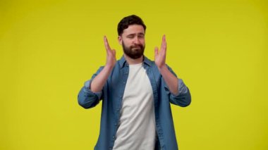 Olumlu sakallı bir adam eğleniyor, dans ediyor, hareketli bir şekilde hareket ediyor, işaret parmaklarını doğrudan kameraya doğrultuyor. Stüdyoda sarı arka planda bir adam var. Kapatın. Yavaş çekim hazır 59.97fps.