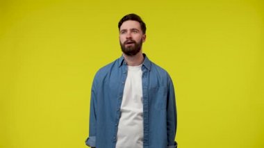 Adam uzaktaki bir şeye zevkle bakar ve elini alnına koyar. Stüdyoda sarı arka planda sakallı bir adam. Kapatın. Yavaş çekim hazır 59.97fps.