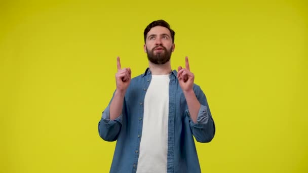 En man tittar på reklamluckan högst upp på skärmen och pekar med två pekfingrar, visar sedan en tumme upp med båda händerna. En man med gul bakgrund. Närbild. Slow motion klar 59,97fps. — Stockvideo