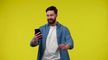 Telefonuyla video görüşmesi yapan bir adam. Adam elini sallayarak müfettişini selamlıyor ve sarı arka planda stüdyodaki bir adamı işaret ediyor. Kapatın. Yavaş çekim hazır 59.97fps.