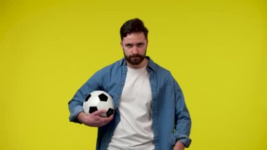 Elinde futbol topu olan yakışıklı sakallı adam, futbol takımını endişelendiriyor ve alkışlıyor, zaferi kutluyor. Stüdyoda sarı arka planda bir adam var. Kapatın. Yavaş çekim hazır 59.97fps.