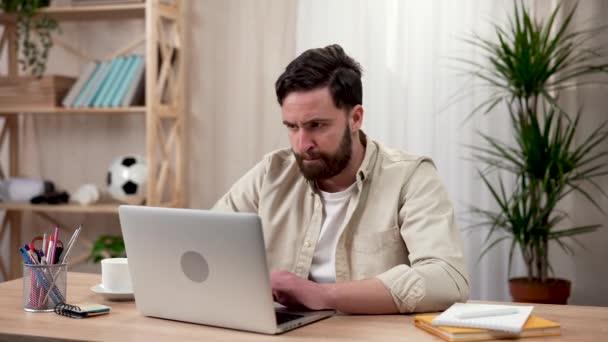 Muž pracuje u laptopu, zatímco sedí doma u stolu. Muž ho popadne za spánky, nejsou tu žádné nápady a myšlenky. Práce na dálku, domácí vzdělání. Zavřít. Zpomalení připraveno 59.97fps. — Stock video