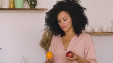 Şirin Afro-Amerikan kadın kese kağıdından aldığı şeyleri alıyor ve tabağa sebze ve meyve koyuyor. Parlak mutfakta poz veren esmer siyah kadın. Kapatın. Ağır çekim hazır, 4K 59.97 fps 'de..