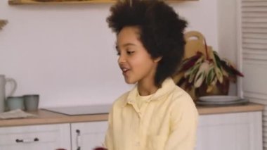 Afro-Amerikan kadın ve kız neşeyle dans ediyor, birbirlerine kırmızı elma atıyor ve sarılıyorlar. Anne ve kızı parlak bir mutfakta poz veriyorlar. Kapatın. Yavaş çekim hazır, 4K 59.97 fps 'de..