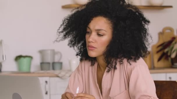 Afroameričanka studuje online, dálkově pracuje s notebookem a přitom si dělá poznámky do sešitu. Černá žena pózuje u stolu v jasné kuchyni. Zavřít. Zpomalení připraveno, 4K při 59,97fps. — Stock video