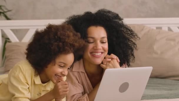 アフリカ系アメリカ人の女性と少女がノートパソコンを使ってビデオ通話で話しています。母と娘のポーズ、明るいインテリアのベッドルームでベッドの上に横たわっていた。閉めろ。スローモーション準備完了、 59.97 fpsで4K. — ストック動画