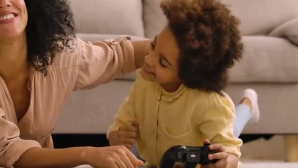 Petite fille afro-américaine joue au jeu sur joystick sans fil et se réjouit de la victoire. Mère et fille couchées sur le sol dans la chambre avec l'intérieur de la maison lumière. Ferme là. Prêt au ralenti, 4K à 59,97 ips. — Video