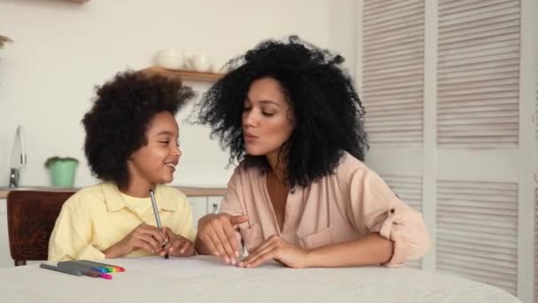 African American litle girl dessine avec des stylos feutre dans l'album. Mère et fille posent assises à table dans une cuisine lumineuse. Une famille heureuse passe du temps ensemble. Prêt au ralenti, 4K à 59,97 ips. — Video