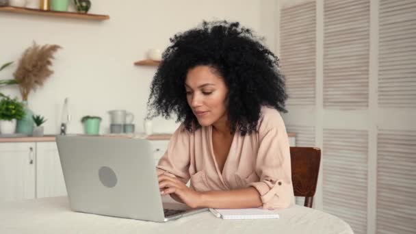 Roztomilá Afroameričanka, soustředěná na přemýšlení, psaní na notebooku, šťastná, že má dobrý nápad. Černá žena pózuje u stolu v jasné kuchyni. Zpomalení připraveno, 4K při 59,97fps. — Stock video
