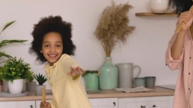 Afro-Amerikalı kadın ve kız neşeyle dans ediyor, şarkı söylüyor ve neşeyle sarılıyorlar. Anne ve kızı parlak bir mutfakta poz veriyorlar. Kapatın. Yavaş çekim.