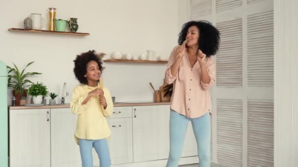 Mujer y chica afroamericanas bailando alegremente, cantando y abrazándose alegremente. Madre e hija posan en una cocina luminosa. Movimiento lento. — Vídeos de Stock