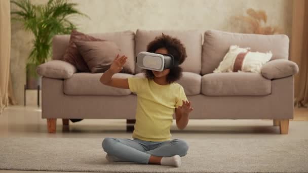 Portrait petite afro-américaine avec casque de réalité virtuelle ou lunettes 3D. Adolescente s'assoit sur le sol dans le hall dans le contexte d'une belle pièce intérieure lumineuse. Mouvement lent. — Video