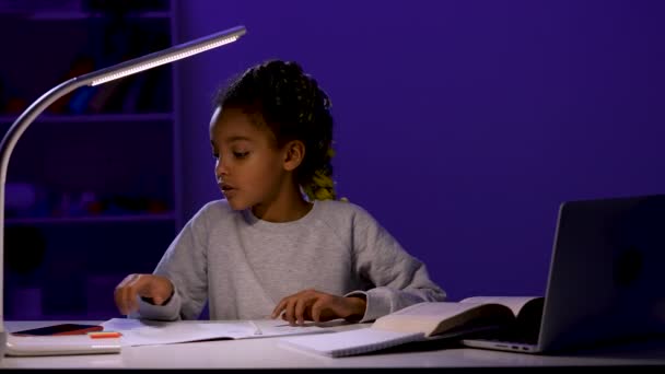 Een schoolmeisje schrijft haar huiswerk, neemt haar telefoon op om berichten te controleren en te antwoorden, en blijft studeren. Een kind aan tafel bij het licht van een nachtlampje. Sluit maar af. Slow motion klaar 59,97 fps. — Stockvideo