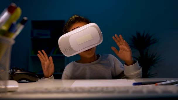 A girl with a virtual reality headset or 3d glasses on her head. The girl sits at a table, turns her head, leans back, playing a virtual game. Close up. Slow motion ready 59.97fps. — Stock Video