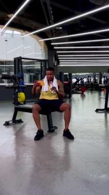 Spor salonunda bir adam telefonuna bakar, su içer, iyi haberi aldığında zaferini kutlamak için dans eder. Arka planda fitness ve vücut geliştirme için spor tesisleri var. Dikey video.