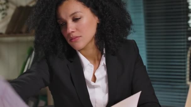 Portret Afroamerykanki przegląda wykresy i wykresy tworzące raport. Bizneswoman pozowanie w miejscu pracy, siedzi przy stole we wnętrzu biura. Zamknij drzwi. Gotowy do zwolnień 59.94fps — Wideo stockowe