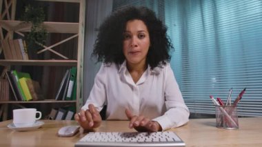 Bilgisayar klavyesinde yazı yazan Afro-Amerikan kadın portresi ve sonra çok sinirli ve sinirli. İş kadını iş yerinde poz veriyor, ofiste masada oturuyor. Webcam görüntüsü. Yavaş çekim hazır 59.94fps.