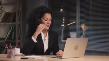 Uzak bir müşteriyi desteklemek için çalışan kulaklık takan Afro-Amerikan kadın portresi. Merkezi ara. İş kadını iş yerinde poz veriyor, ofiste masada oturuyor. Yavaş çekim hazır 59.94fps.