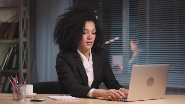 Retrato de mujer afroamericana termina el trabajo, cierra el portátil y se va. Empresaria posando en el lugar de trabajo, sentada en la mesa en el interior de la oficina. Cámara lenta lista 59.94fps. — Vídeo de stock