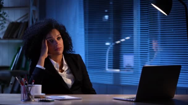 Portræt af træt afrikansk amerikansk kvinde på baggrund af tænde og slukke lyset. Forretningskvinde poserer på arbejdspladsen, sidder ved bordet i det indre af kontoret. Langsom bevægelse klar 59.94fps. – Stock-video