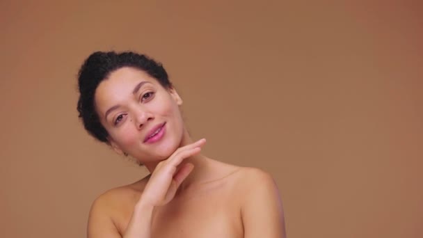 Beauty portret van jonge Afro-Amerikaanse vrouw, ze zachtjes raakt gezicht met haar vingers. Zwart vrouwelijk model poserend op bruine studio achtergrond. Slow motion klaar, 4K bij 59,94fps. — Stockvideo