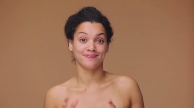 Genç Afrikalı Amerikalı bir kadının güzel portresi bir sürü ilginç bilgi veriyor ve anlatıyor. Kahverengi stüdyo arka planında poz veren siyah bir kadın model. Yavaş çekim hazır, 4K 59.94fps 'de..
