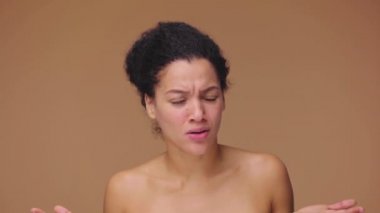 Afro-Amerikalı genç bir kadının güzel portresi üzgün, hayır diyor ve olumsuz bir şekilde başını sallıyor. Kahverengi stüdyo arka planında poz veren siyah bir kadın model. Yavaş çekim hazır, 4K 59.94fps 'de..